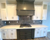 Kitchen featuring backsplash, wood-type flooring, custom range hood, and white cabinetry