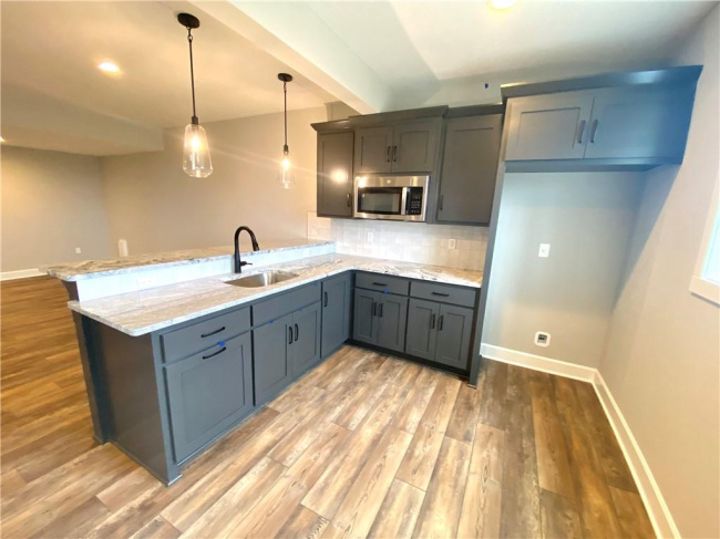 Kitchen with sink, tasteful backsplash, light wood-type flooring, hanging light fixtures, and kitchen peninsula